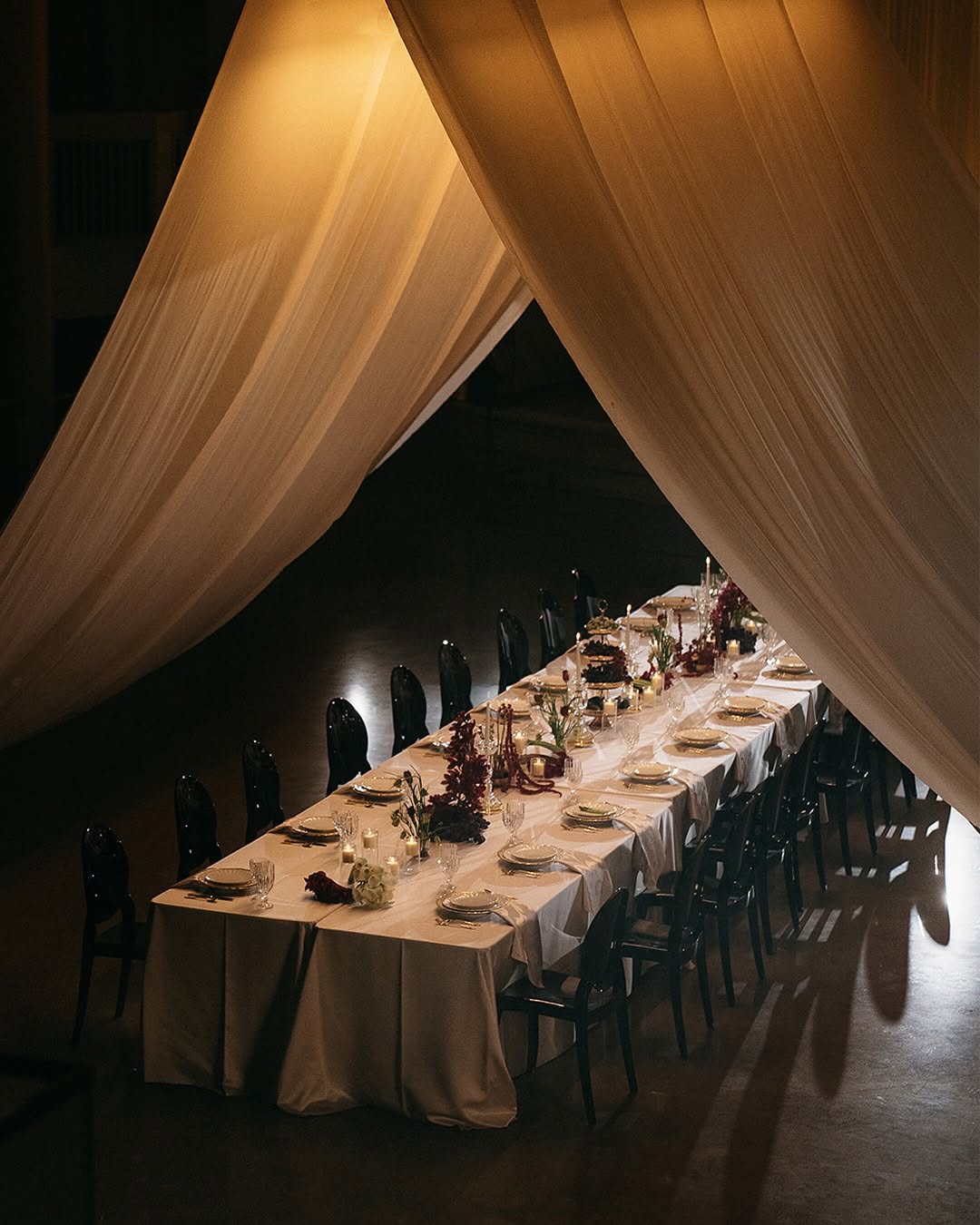 Long candlelit dinner table beneath sweeping sheer drapery