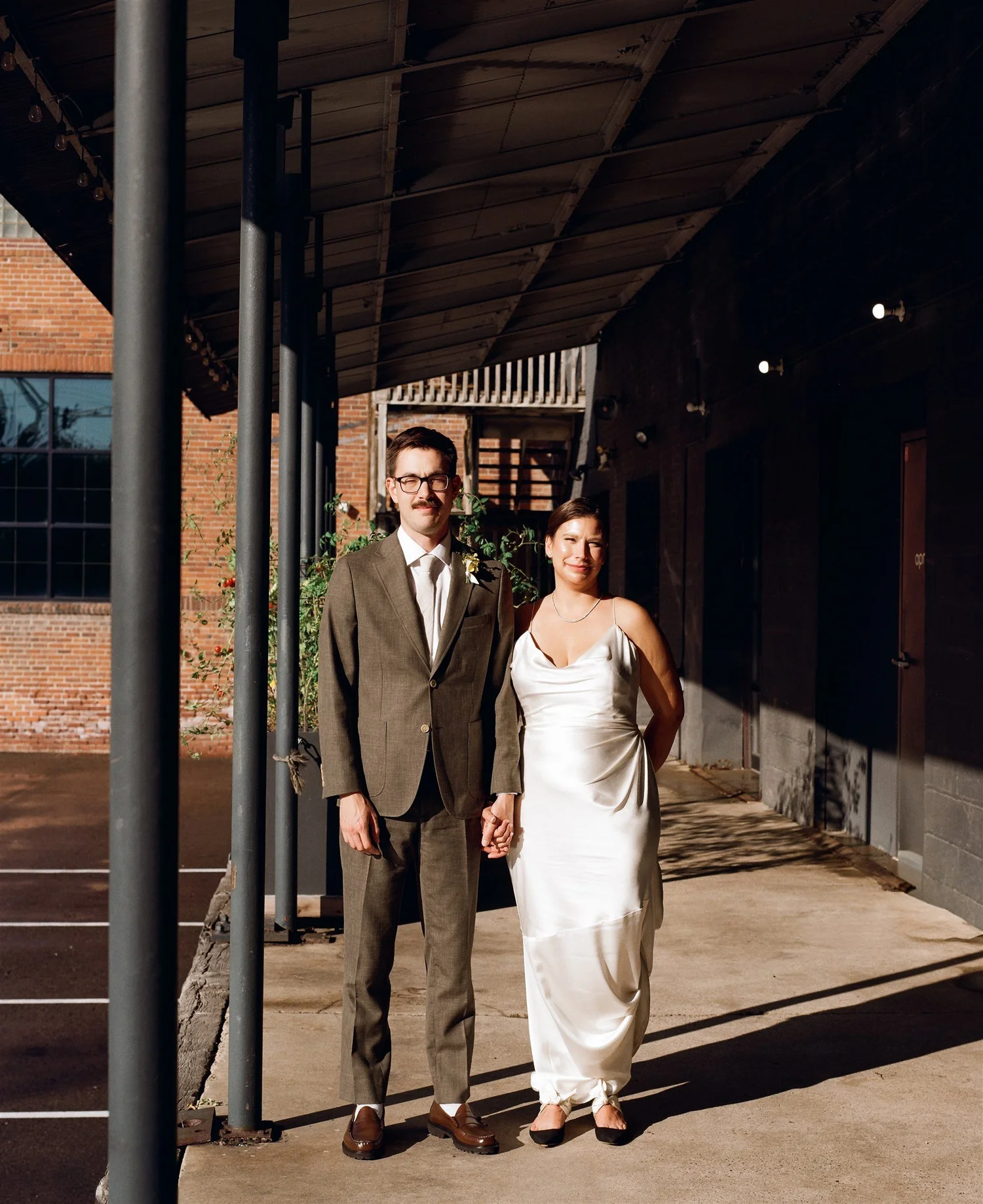 A couple holding hands in golden-hour light beneath an industrial canopy, shot on film