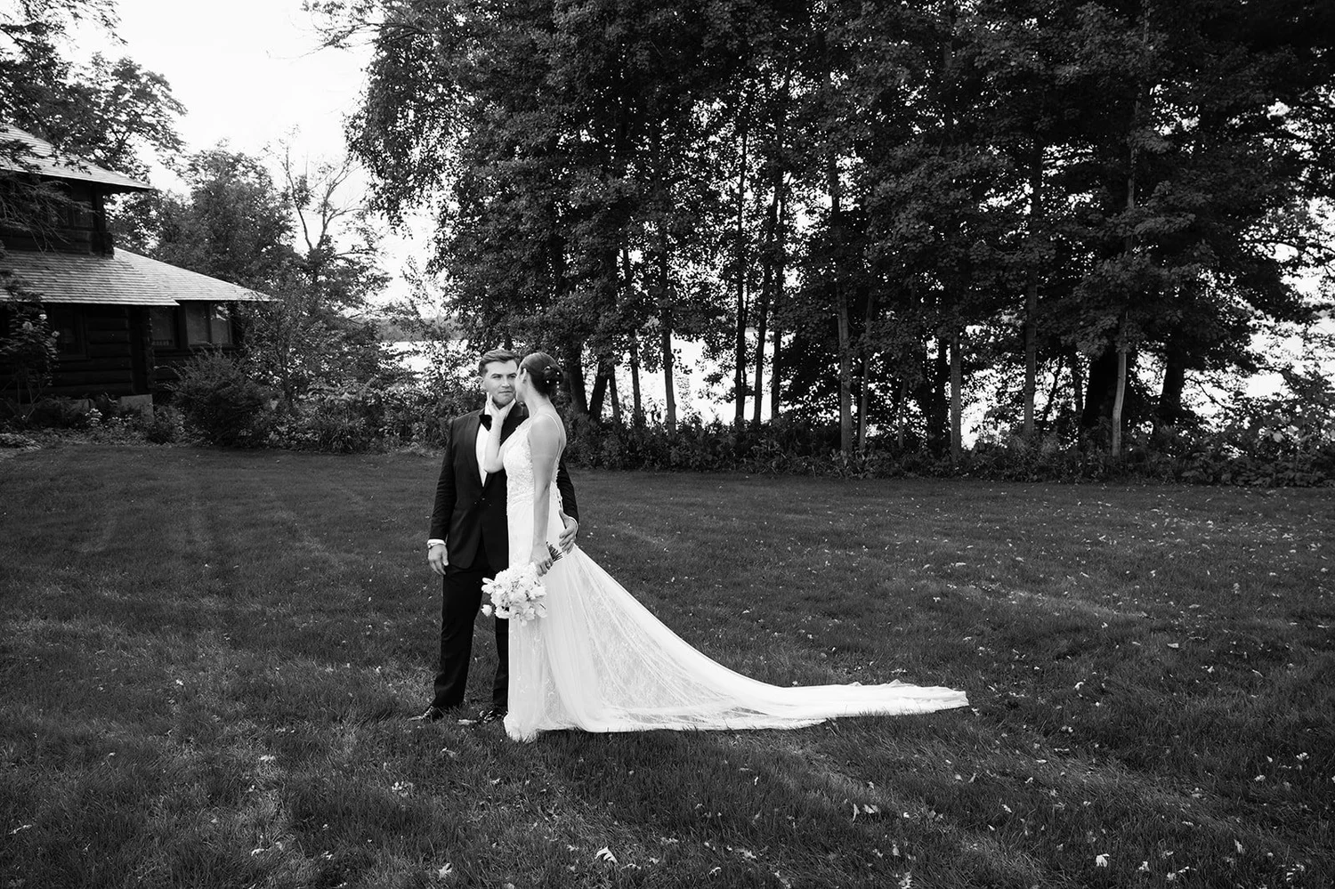 A couple on the lakeside lawn at Stout's Island Lodge, her train sweeping the grass — black and white
