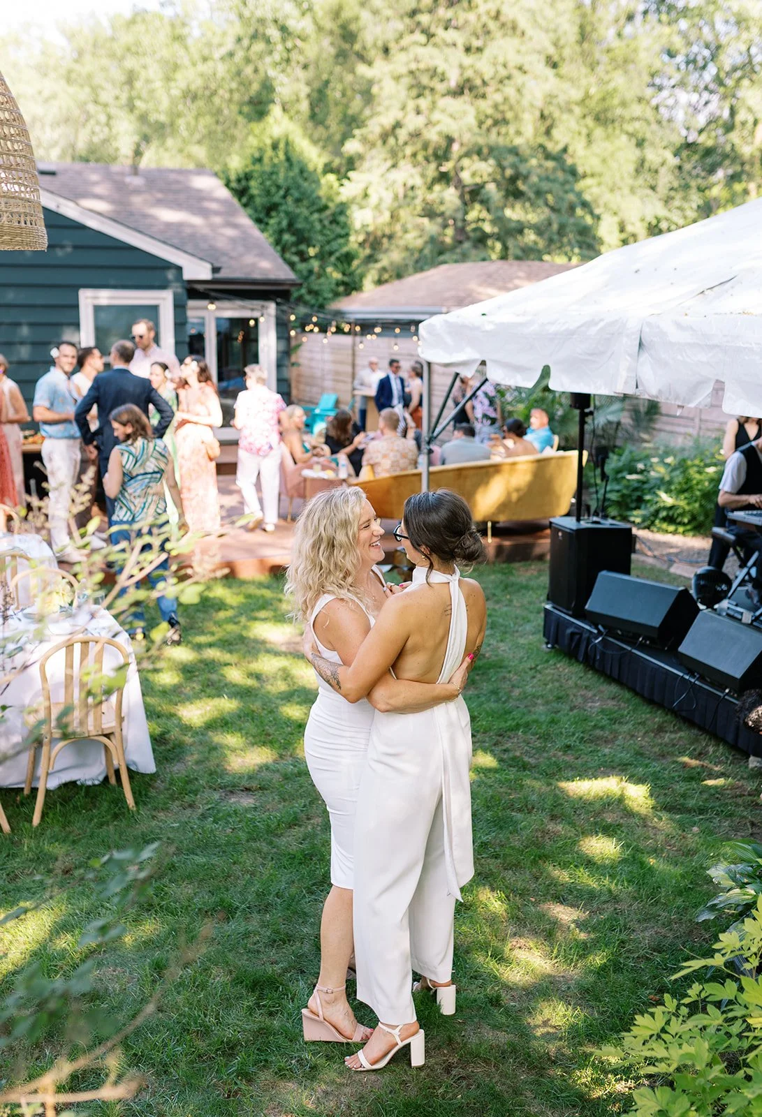 Ali and Alyson dancing together in white at their backyard wedding, guests and a live band around them