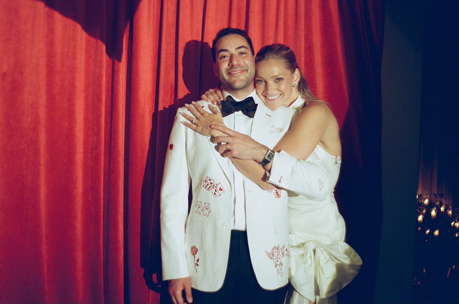Bailey wrapping her arms around Ameen in front of the red theater curtain, his white jacket embroidered with dice and cherubs — shot on film