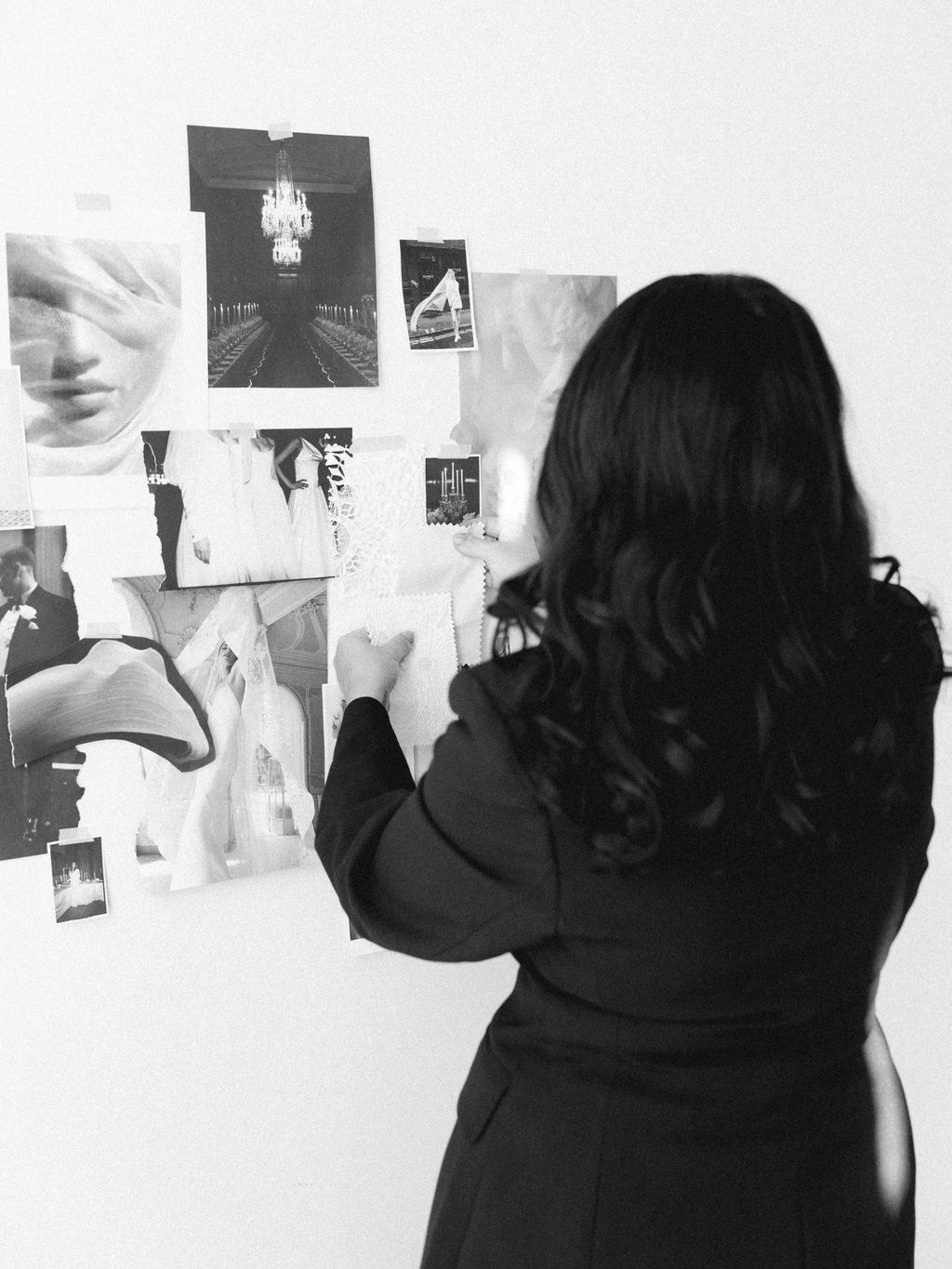 Steph pinning black and white imagery to a moodboard wall, photographed from behind