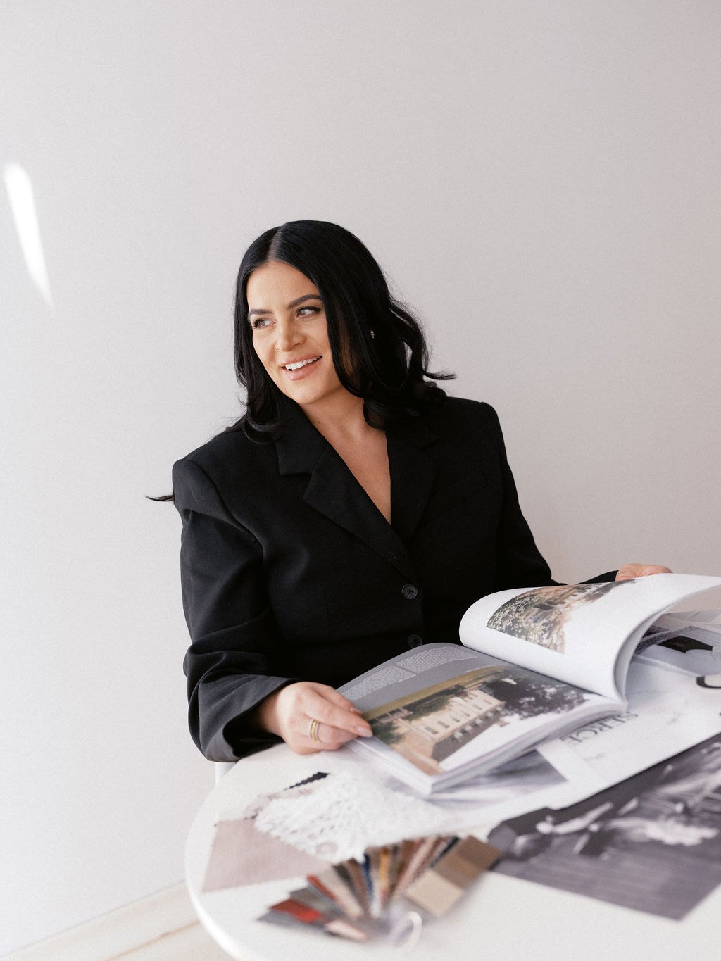 Steph in the studio, smiling over an open design book with fabric swatches on the table