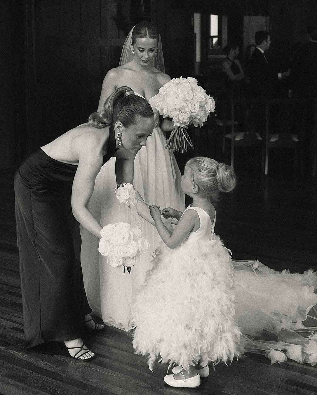 Three generations of women — a bride, her mother, and a flower girl — share a quiet moment in black and white